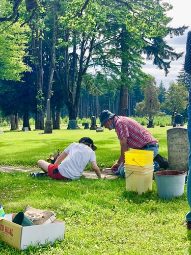young boy and grandfather clean grave of family who served in the military